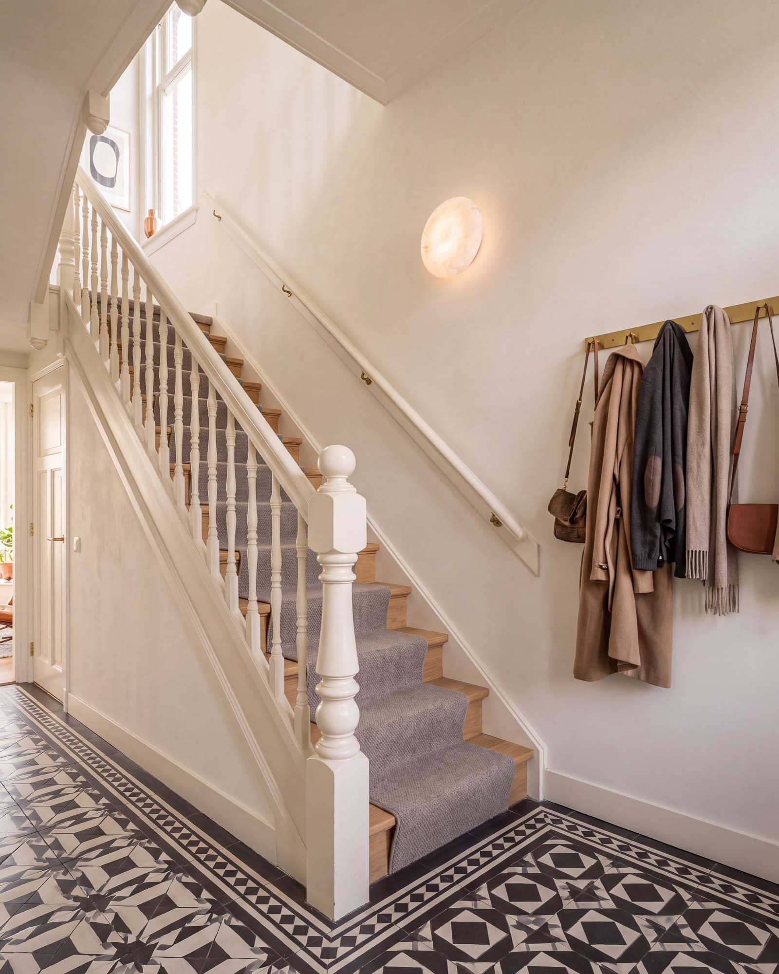 Gerestaureerde trappenhal met witte balustrade, eiken treden en zwart-witte tegelvloer
