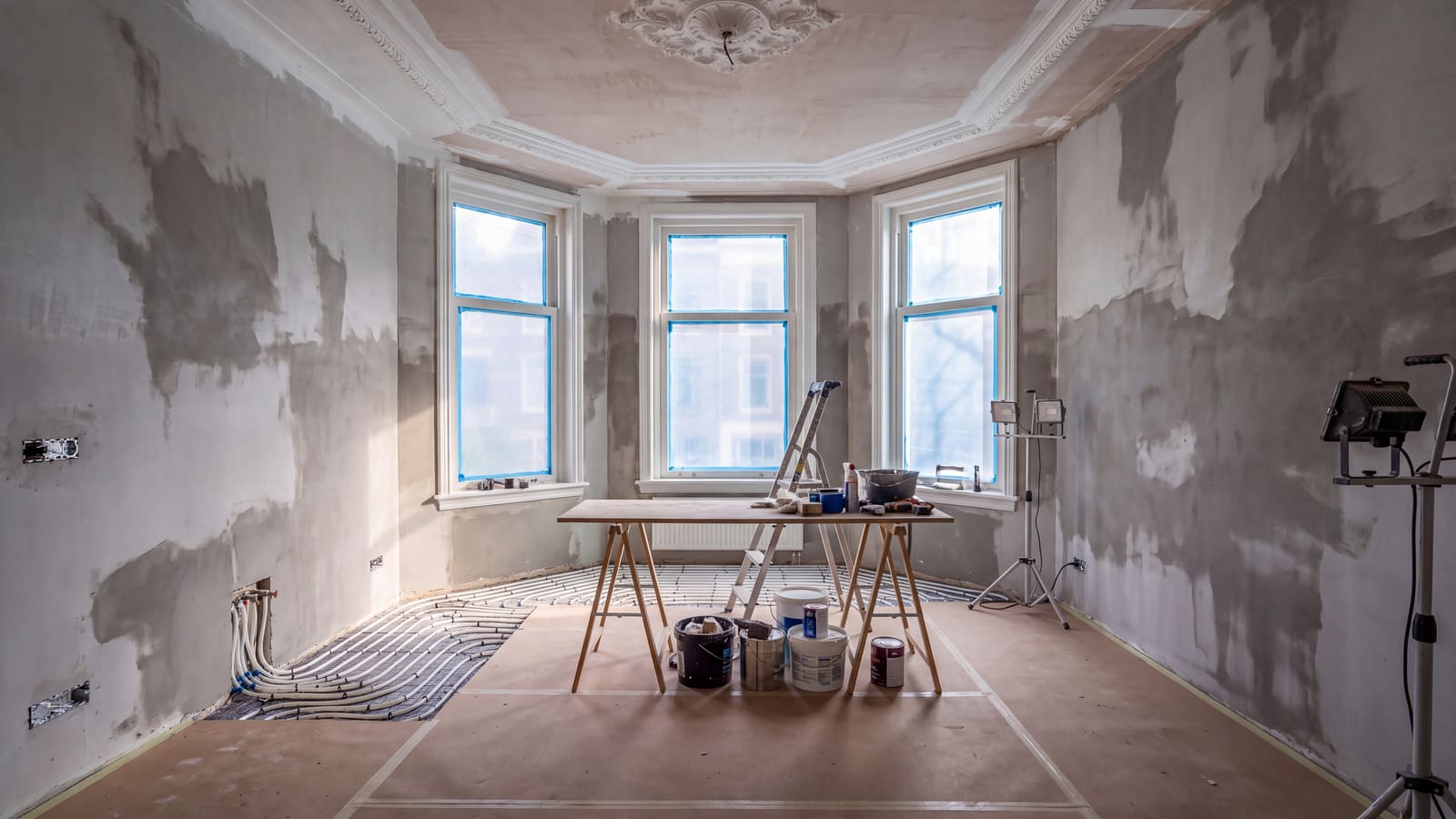 Dezelfde woonkamer tijdens de afbouw: vers stucwerk, nieuwe installaties en afgeschermde vloer